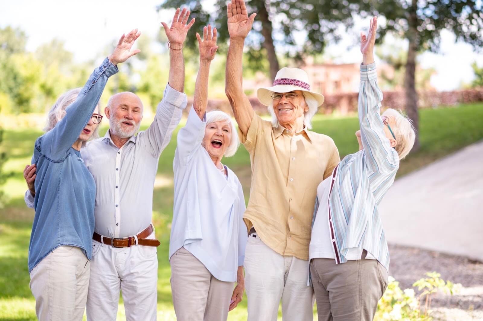 A group of older adult friends embracing and raising their hands while outdoors.