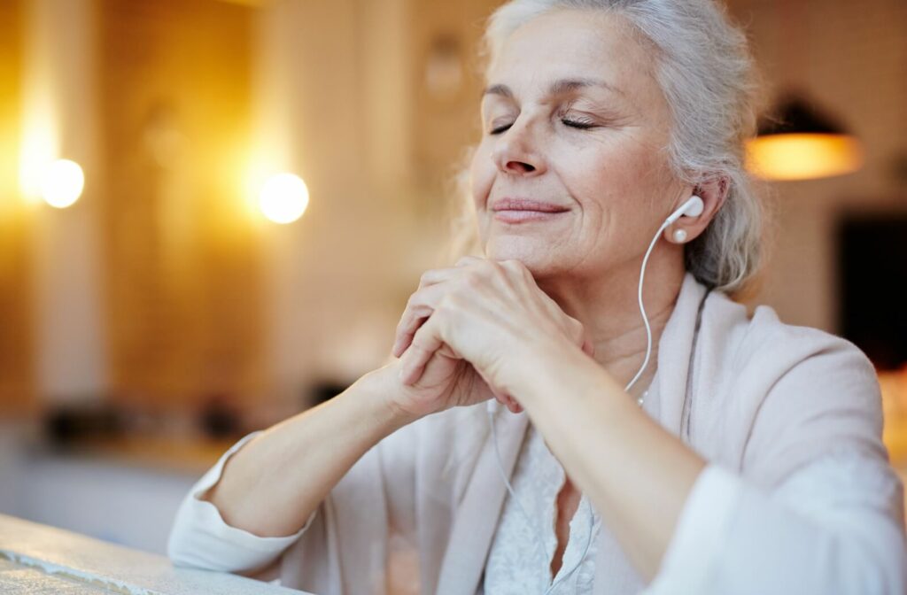A senior smiles while they relax, listening to music with earbuds.